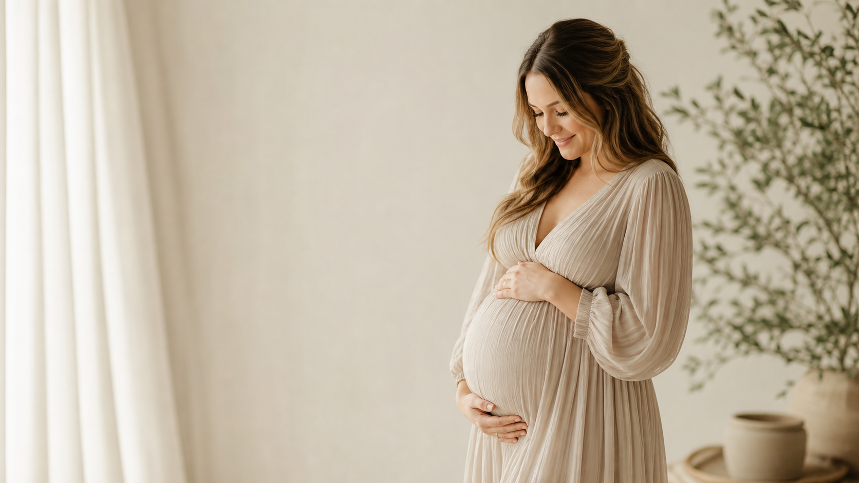Expectant mother in a flowing cream dress cradling her bump
