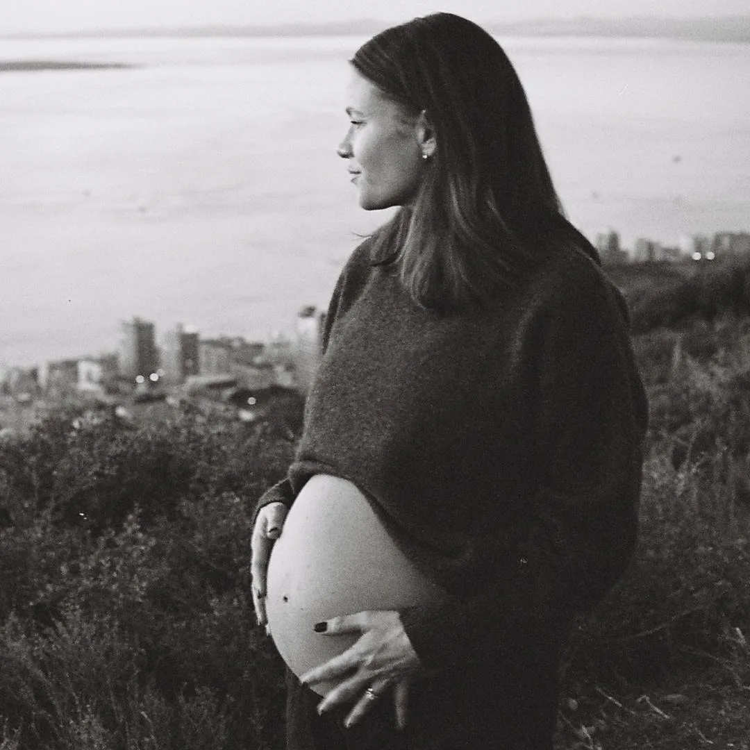 Expectant mother cradling her bump, overlooking the city and bay at dusk